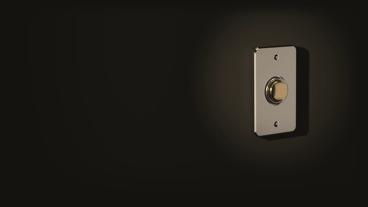 Une sonnette sur un mur sombre : une platine métallique, un bouton couleur laiton